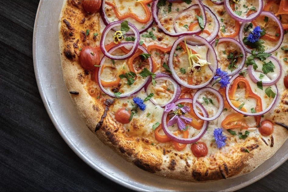 Vegetable pizza with red onion, cherry tomatoes, herbs, and edible flowers (cropped)